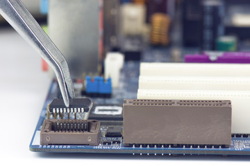 Tweezers Holding And Assembling Black Microchip On Computer Motherboard Closeup 