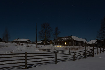 Wooden country houses in snow at winter night under blue dark sky