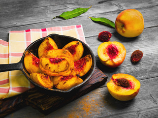 Baked peaches on a cast iron pan, leaf, cinnamon, spices for baked peaches. Fresh red fruit yellow peaches for baking, gray wooden background, board. Top view, flat lay. 