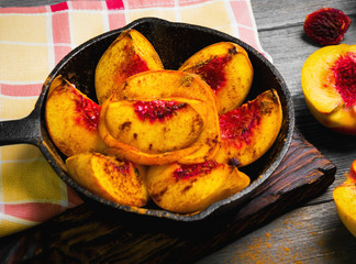 Baked peaches on a cast iron pan, leaf, cinnamon, spices for baked peaches. Fresh red fruit yellow peaches for baking, gray wooden background, board. Top view, flat lay. 