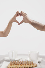 Cropped image of couple making heart shape sign while having coffee against white background