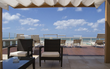 roof in front of the sea with tanned beds, armchais, blue sky and white clouds