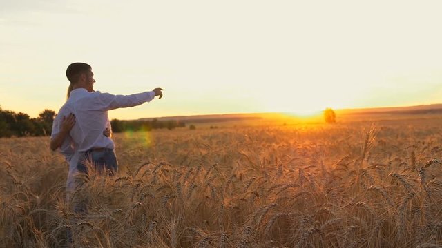 Young beautiful couple in a wheat field. Silhouette on sunset background. Slow motion