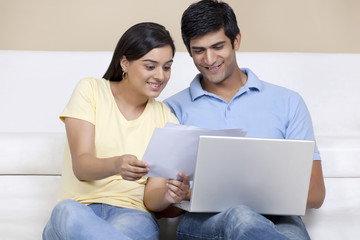 Fototapeta premium Young Indian couple reading document while using laptop 