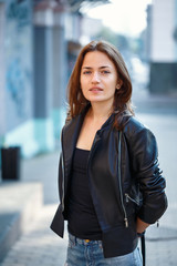 Portrait of a girl in a leather jacket standing on a city street