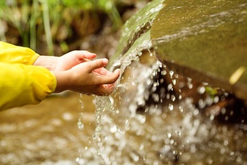 Child washing hands in fresh, cold, potable water of mountain spring