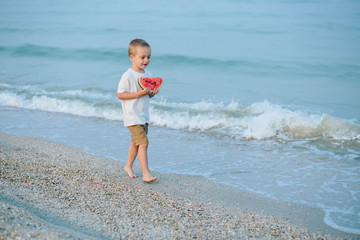 Happy child on the beach and eating watermelon outdoors