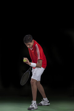 Male tennis player preparing to serve over black background