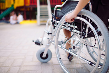 Fototapeta premium A girl with a broken leg sits in a wheelchair in front of the playground.