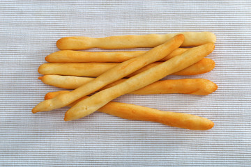 Seven bread sticks lying on a cotton tablecloth.