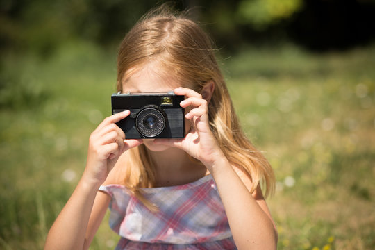 Little girl taking pictures with vintage camera. Young photographer girl making shots outdoors.