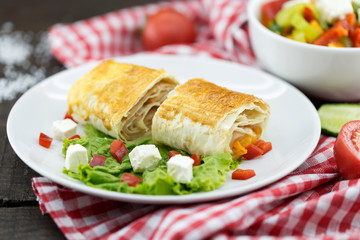 Lavash rolls with meet, vegetables and cheese served with green lettuce salad, feta chesse and red pepper on rustic wooden table. Healthy breakfast concept