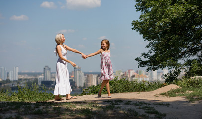 Naklejka na ściany i meble Mom and daughter together. Mother and daughter holding hands, walking in city park.