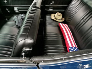 Sternenbanner und Cowboyhut auf der schwarzen Sitzbank eines amerikanischen Coupé der Sechziger...