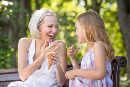 Mom and daughter eating ice cream together. Young mother laughing, holding ice cream.