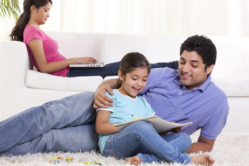 Young father assisting child in drawing with woman sitting in the background 