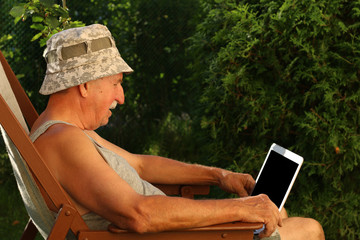 Grandfather sitting in garden with laptop, side view