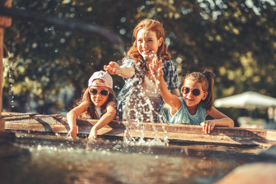 Mother and her daughters playing in the city square fountain. They sprayed with water. Refreshing on a hot summer day.	