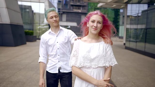 young pretty girl in a white dress with her hair dyed pink meets with her lover on a city street. men blue hair