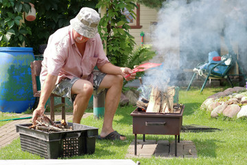 Grandfather lights the fire in the garden for cooking