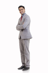 Full length portrait of happy young businessman with arms crossed standing against white background 