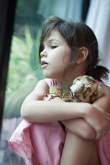 Lonely sad asian girl sits near a window with her favorite toy