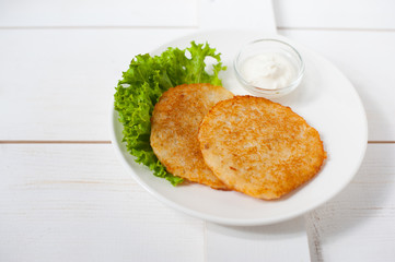 Fried potato pancakes with sour cream and fresh leaf salad on a white plate