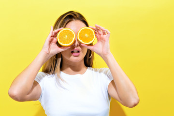 Happy young woman holding oranges halves on a yellow background