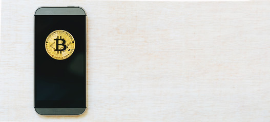 Gold bitcoin cryptocurrency with a smartphone on a wooden table