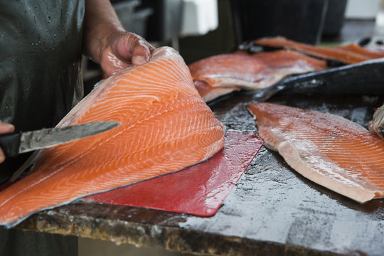 Fishmonger hands cutting whole salmon fish into big fillets