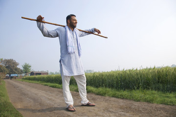 Full length of an Indian man standing with a stick across his shoulders 