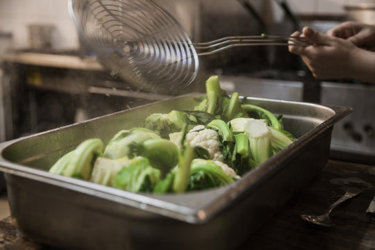 Hands placing boiled cauliflower in a metal roasting tray