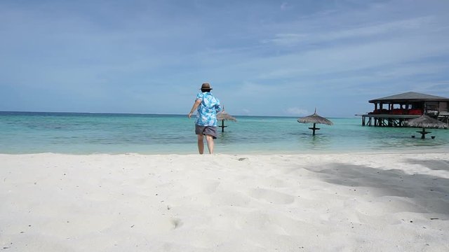 Asian tourist running to beautiful Maldives clear sea. Enjoying her vacation at luxury resort