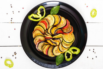 Fried zucchini slices, eggplant, tomato on a black plate on a white background. Ratatouille.