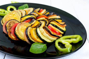 Fried zucchini slices, eggplant, tomato on a black plate on a white background. Ratatouille.