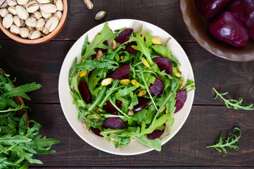 Vegan vegetable vitamin salad from beets, arugula and pistachios on a dark wooden background.