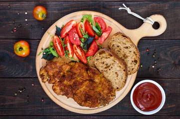 Juicy schnitzel with ciabatta, tomato salad on a dark wooden background. Top view.
