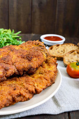 A large Viennese schnitzel on a dark wooden background. Vertical view