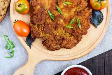 A large Viennese schnitzel on a cutting board on a dark wooden background. Top view.