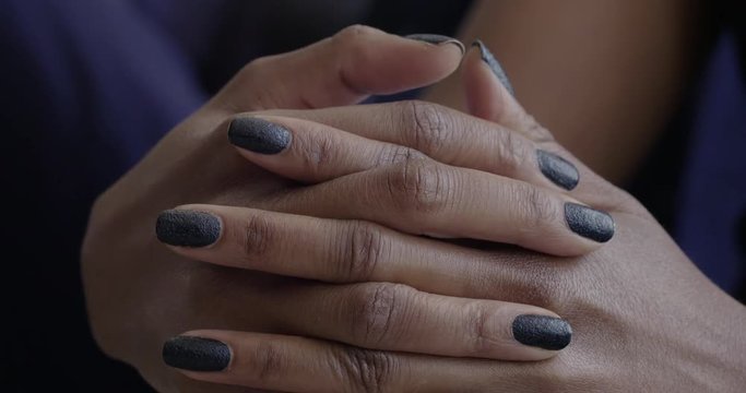 African American woman's hands with dark, glittering nail polish, clasped together across her knee in natural light. Slow motion 4K, recorded at 60fps.