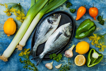 Dorado in baking form ready to cooking, preparation on rustic blue background with fresh vegetables, herbs and spices. Top view, overhead