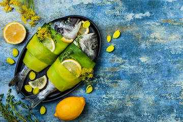 Dorado wrapped in leek in baking form ready to cooking, preparation on rustic blue background with oil, herbs and spices. Top view, overhead, copy space