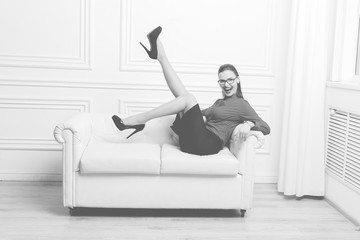 Obraz premium Attractive brunette businesswoman in eyeglasses lying on white sofa as symbol of sex, seduction, business, work, success, style, leadership, management, entrepreneur, Monochrome image