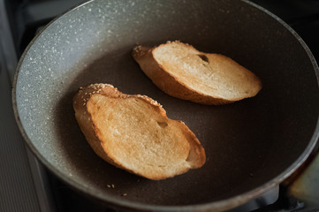 Two pieces of toasted bread. Toasted bread lies on a kitchen wooden board on a dark table. Bread with cheese, garlic, herbs and tomatoes.