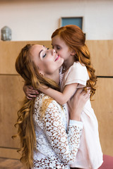 beautiful happy mother and cute redhead daughter hugging indoors