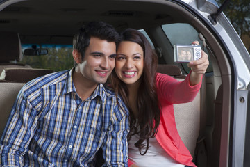 Fototapeta premium Young man and young woman sitting in the trunk of a car