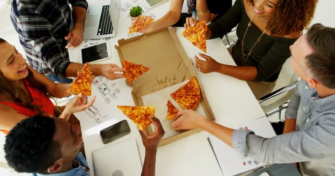 Happy African American and mixed-race executives sharing pizza in conference room at office