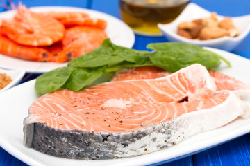 raw salmon, shrimps, nuts and olive oil on wooden background