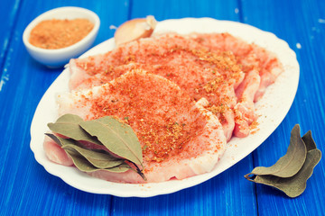 raw pork with herbs on white dish on wooden background