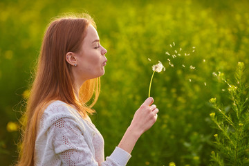 redheaded teen girl blowing on dandelions